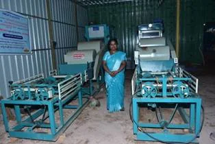 अल्लम गौतमी नारियल रेशा उत्पाद बनाने वाली मशीनों के बीच अपनी इकाई में खड़ी हैं।